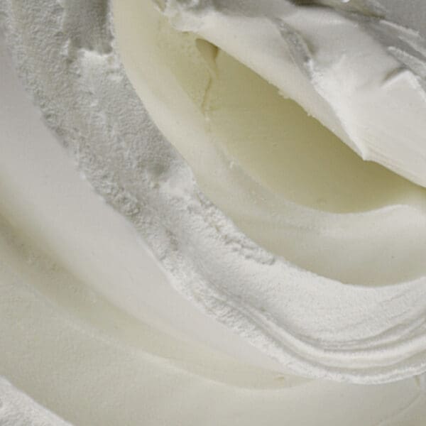 Close-up of the smooth, creamy white texture with swirls and folds akin to thick whipped cream or frosting, accentuated by soft lighting that creates gentle shadows and contours, reminiscent of the rich consistency of Elenka Cremox 298 Ice Cream Emulsifier and Stabilizer (20x1Kg case).