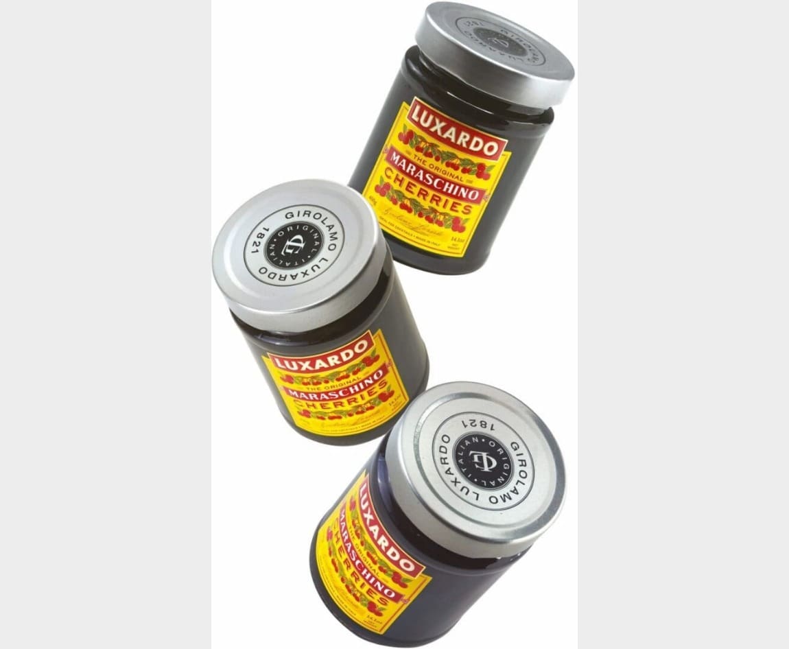 Three jars of Luxardo maraschino cherries with yellow and red labels are arranged diagonally on a light gray background.