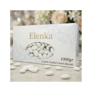 A box labeled “Elenka” contains white confetti candied coated almonds. Some almonds are scattered on a light surface, with blurred flowers in the background. The box weighs 1000 grams.